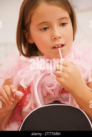 Ein Mädchen trägt eine rosafarbene Federboa und trägt Lippenglanz auf Stockfoto