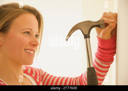 Eine Frau, die einen Nagel in eine Wand schlägt Stockfoto