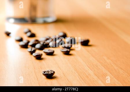 Detail der Kaffeebohne mit unfokussierter Kaffeekanne auf Holzhintergrund Stockfoto