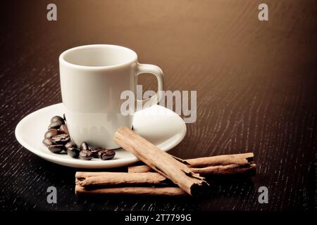 Weiße Tasse mit Kaffee in der Nähe von Kaffeebohnen über Holztisch in der Nähe von Zimt Stockfoto