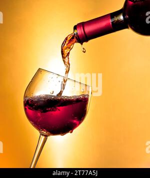 Rotwein in das auf goldenem Hintergrund geneigte Glas gießen Stockfoto