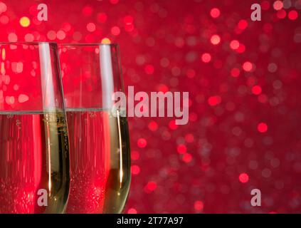 Zwei Sektflöten geben Anfeuerungen auf rotem Bokeh-Hintergrund mit Platz für Text Stockfoto