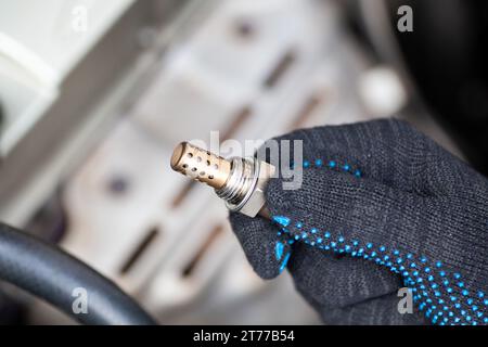 Sauerstoffsensor für Benzin- und Dieselmotoren in der Hand gegen Pkw-Motor. Der Mechaniker hält den Sauerstoffsensor. Lambdasonde. Stockfoto