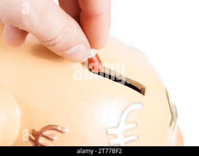 Hand, die eine rote Pille in eine Schweinebank auf weißem Hintergrund mit Platz für Text einfügt, Konzept für Sparkosten Stockfoto