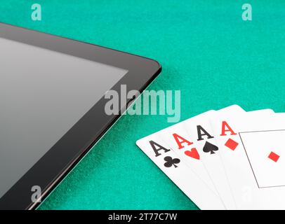 Pokerkarten in der Nähe eines digitalen Tablet-pcs auf grünem Spieltisch, Konzept des Poker online Stockfoto