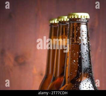 Drei Flaschen frisches Bier mit Tropfen auf Holzhintergrund Stockfoto