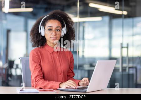 Ernsthafte, konzentrierte Frau, die im Büro mit einem Laptop arbeitet, Geschäftsfrau denkt mit Kopfhörern, die auf der Tastatur tippen und auf die Kamera schauen, Programmierer-Entwickler hören Audio-Podcasts. Stockfoto