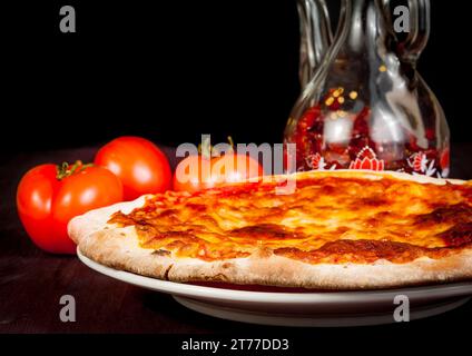 Italienische Pizza in der Nähe von Tomaten und würzigem Öl auf Holztisch, typisch italienische Pizza Stockfoto