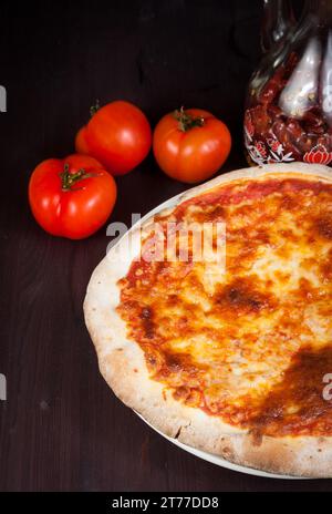 Köstliche frische Pizza in der Nähe von Tomaten und scharfes Öl auf Holztisch Stockfoto