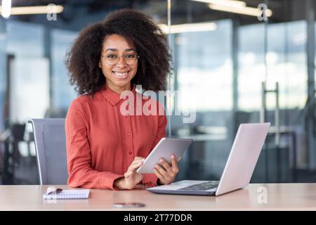 Porträt fröhliche erfolgreiche Geschäftsfrau am Arbeitsplatz im Büro, weibliche Mitarbeiterin lächelt und in die Kamera blickt, am Tisch mit Laptop sitzt, Tablet am Arbeitsplatz verwendet, zufriedene Leistungsergebnisse. Stockfoto