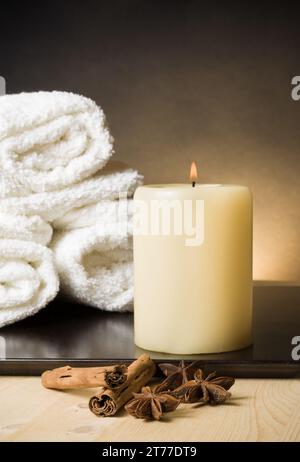 Spa-Massage-Hintergrund mit Handtuch und Kerze mit Gewürzen und Zimtgeschmack, warme Atmosphäre Stockfoto