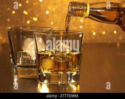 Barkeeper, der Whiskey vor leerem Whiskyglas auf goldenem Bokeh gießt Stockfoto