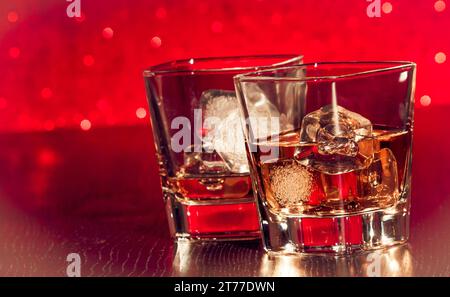 Whiskey-Glas mit Eis vor leerem Whiskey-Glas auf rotem Bokeh Stockfoto