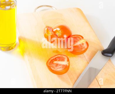 Blick von oben auf frische, reife Kirschtomaten auf einem alten Schneidebrett. Flasche Olivenöl im Hintergrund auf weiß Stockfoto