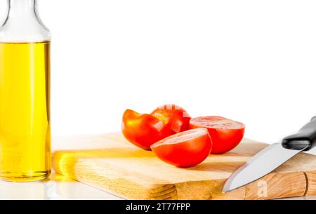 Frische, reife Kirschtomaten auf einem alten Schneidebrett. Flasche Olivenöl im Hintergrund auf weiß Stockfoto