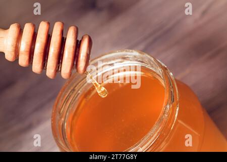 Honigglas auf Holztisch mit Honighölzer Pendel oben mit Tropfenhonig Stockfoto