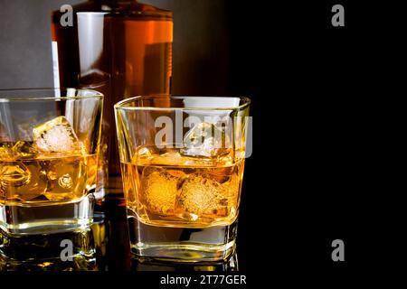 Whiskey mit Eis in Gläsern vor der Flasche auf schwarzem Hintergrund, mit Reflexion Stockfoto