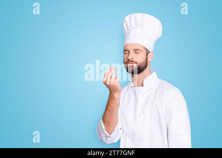 Porträt mit Kopierraum, leerer Platz für Werbung, Produkt eines attraktiven Kochs in Baskenmütze mit geschlossenen Augen, weißes Outfit, das Bellisimo-Symbol macht Stockfoto