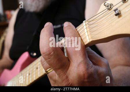 Die Hand eines Mannes, der einen Akkord auf einer rosa Gitarre mit Stahlsaiten spielt Stockfoto