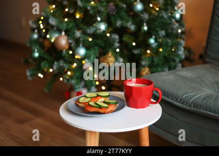 Weihnachts-Snack. Eine helle Tanne neben Sandwiches und einer roten Tasse Kaffee Stockfoto