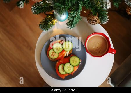 Weihnachts-Snack. Eine helle Tanne neben Sandwiches und einer roten Tasse Kaffee Stockfoto