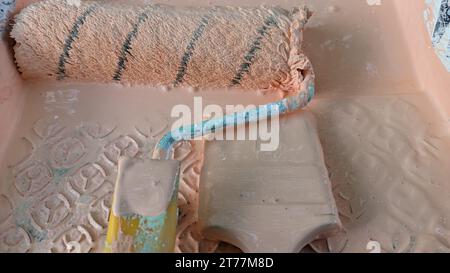 Rolle und Pinsel verschmutzt im Farbständer in einer Badewanne mit Farbe Stockfoto