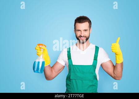 Porträt des fröhlichen Reinigungsmittels in Uniform mit Stoppeln in der Hand, mit Daumen-nach-oben-Taste ja fertig Empfehlen mit dem Finger Stockfoto