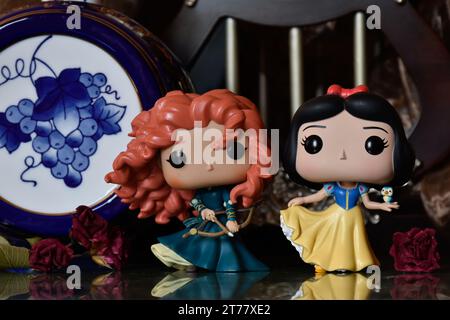 Funko Pop Actionfiguren der Disney Prinzessinnen Merida (tapfer) und Schneewittchen. Mittelalterliche Burg, fabelhaftes Königreich, rote Rosen, Porzellan blaues Fass. Stockfoto