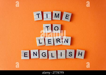 Zeit, Englisch zu lernen. Motivation. Der Satz ist in Holzbuchstaben von oben angeordnet. Motivation. Orangefarbener flacher Lay-Hintergrund Stockfoto