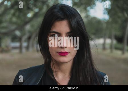 Eine junge Frau, die eine schwarze Jacke und einen rosa Lippenstift trägt, während sie in die Kamera schaut Stockfoto