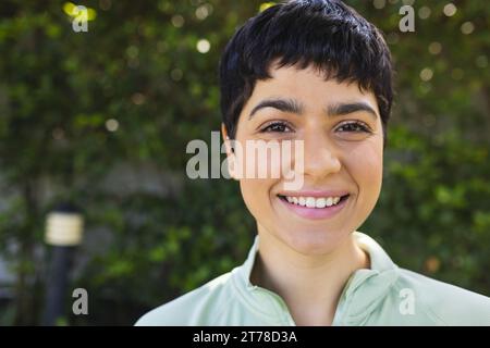 Porträt einer glücklichen birassischen Frau mit kurzen dunklen Haaren, die im sonnigen Garten lächelt Stockfoto