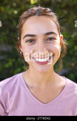 Porträt einer glücklichen Frau mit langen braunen Haaren, die im sonnigen Garten lächelt Stockfoto