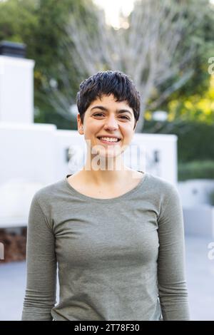 Porträt einer glücklichen birassischen Frau mit kurzen dunklen Haaren, die lächelnd auf der Gartenterrasse steht Stockfoto