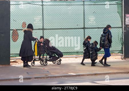 Eine ausgedehnte orthodoxe jüdische Familie spaziert an einem kühlen Herbsttag im Jahr 2023 an einer Baustelle vorbei. In Williamsburg, Brooklyn, New York City. Stockfoto