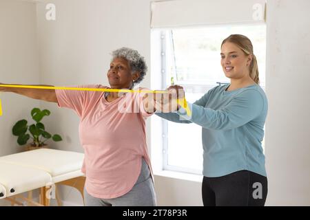 Kaukasische Physiotherapeutin und ältere afrzianische amerikanische Patientin mit Band, Kopierraum Stockfoto