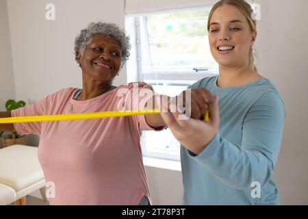 Kaukasische Physiotherapeutin und ältere afrzianische amerikanische Patientin mit Band, Kopierraum Stockfoto