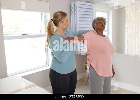 Kaukasische Physiotherapeutin und ältere afrzianische amerikanische Patientin, die sich dehnt, Kopierraum Stockfoto