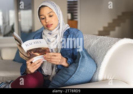 Birassische Frau im Hijab, die Buch im Wohnzimmer liest Stockfoto