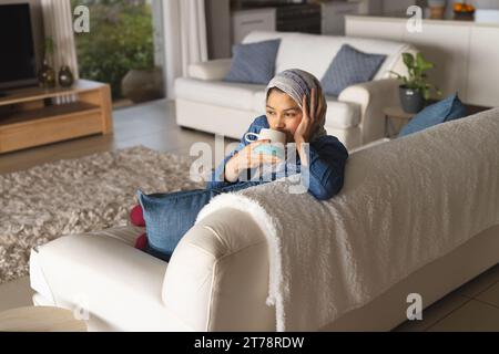 Birassische Frau im Hijab trinkt Kaffee im Wohnzimmer Stockfoto