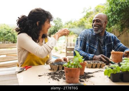 Glückliches reifes, vielfältiges Paar, das Spaß mit Wasserspray hat, Pflanzen auf der Gartenterrasse topft Stockfoto