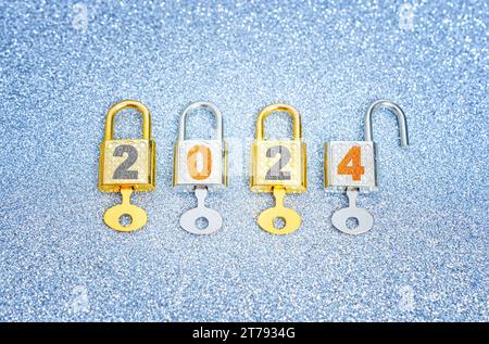 Das neue Jahr 2024 wird eröffnet: Reihe von vier beschrifteten Vorhängeschlössern mit Hauptschlüsseln auf einem funkelnden Hintergrund. Stockfoto
