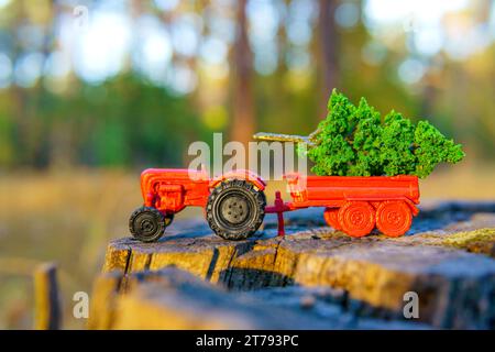 Miniaturwelt: Winziger Traktor mit einem riesigen grünen Baum im Bett parkt auf einem Baumstumpf in einer Waldlandschaft. Stockfoto