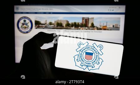 Person, die ein Mobiltelefon mit dem Siegel der United States Coast Guard (USCG) vor der Webseite hält. Schwerpunkt auf dem Display des Telefons. Stockfoto