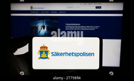 Person mit Smartphone und Logo des schwedischen Sicherheitsdienstes Säkerhetspolisen (SÄPO) vor der Website. Schwerpunkt auf dem Display des Telefons. Stockfoto