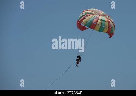 Zwei Personen - Mann und Kind fliegen. Bunter Fallschirm, der Mann hält hinter einem Kind. Nahaufnahme des Fotos am klaren blauen Himmel Stockfoto