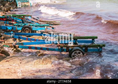 Viele bunte, hölzerne Jetski-Anhänger parkten am Sandstrand in der Nähe großer Steine, die teilweise von Flut bedeckt sind. Tropisches Thailand Stockfoto