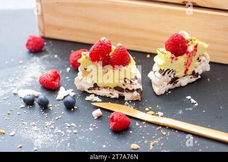 Nahaufnahme von Mini-pavlova-Kuchen mit Pistazien- und Schokoladenfüllung. Desserts mit Schlagsahne und frischer Himbeere Stockfoto