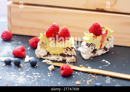 Nahaufnahme von Mini-pavlova-Kuchen mit Pistazien- und Schokoladenfüllung. Desserts mit Schlagsahne und frischer Himbeere Stockfoto