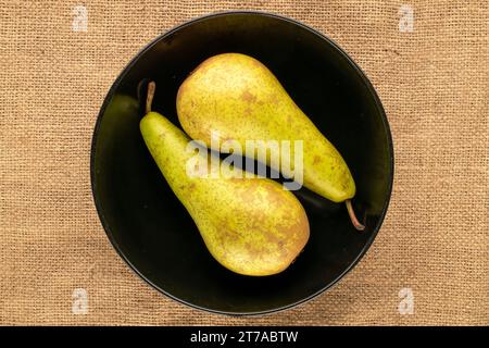 Zwei reife Birnen mit schwarzer Keramikplatte auf Jutetuch, Makro, Draufsicht. Stockfoto