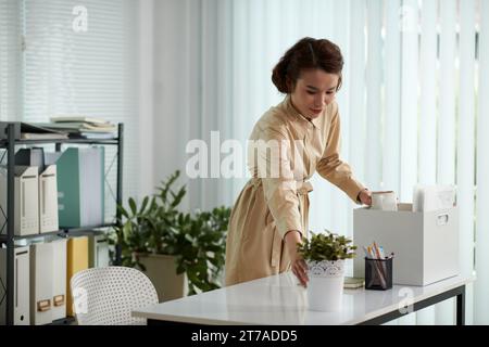 Eine junge Geschäftsfrau, die in einem neuen Büro Sachen aus der Kiste herausnimmt Stockfoto
